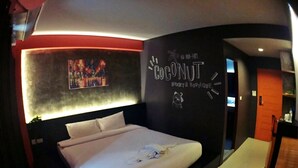 A modern hotel room with a large bed, a headboard with a mural, and a wall with the text "COCONUT BUDGET & BOUTIQUE". - Coconut Budget and Boutique Huahin (Hua Hin)