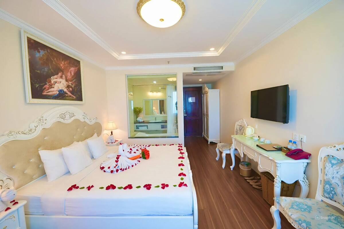 A hotel room with a large bed, a desk, a television, and a mirror.