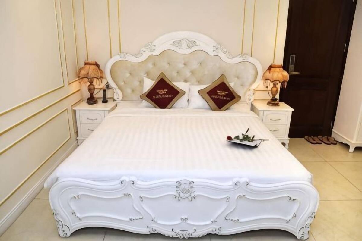 A large bed with ornate headboard, two bedside tables, and two lamps.