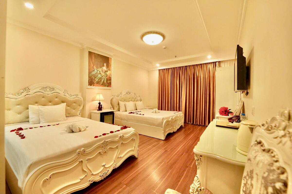 A hotel room with two beds, a desk, a television, and a painting on the wall.