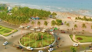 A coastal cityscape with a beach, palm trees, and a roundabout with vehicles. - Tuyet Son Hotel (Da Nang)