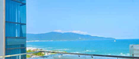 Un balcone con vista sull'oceano, una montagna all'orizzonte e un edificio con finestre blu.
