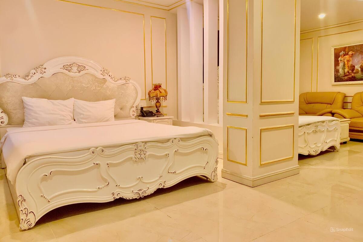 A luxurious bedroom with a large ornate bed, a matching nightstand, and a yellow armchair.