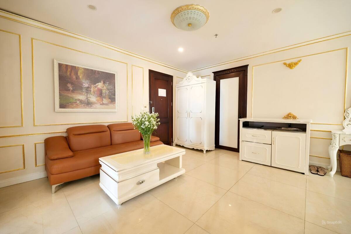 A well-lit living room with a brown sofa, a white coffee table with a vase, a white cabinet, and a painting on the wall.
