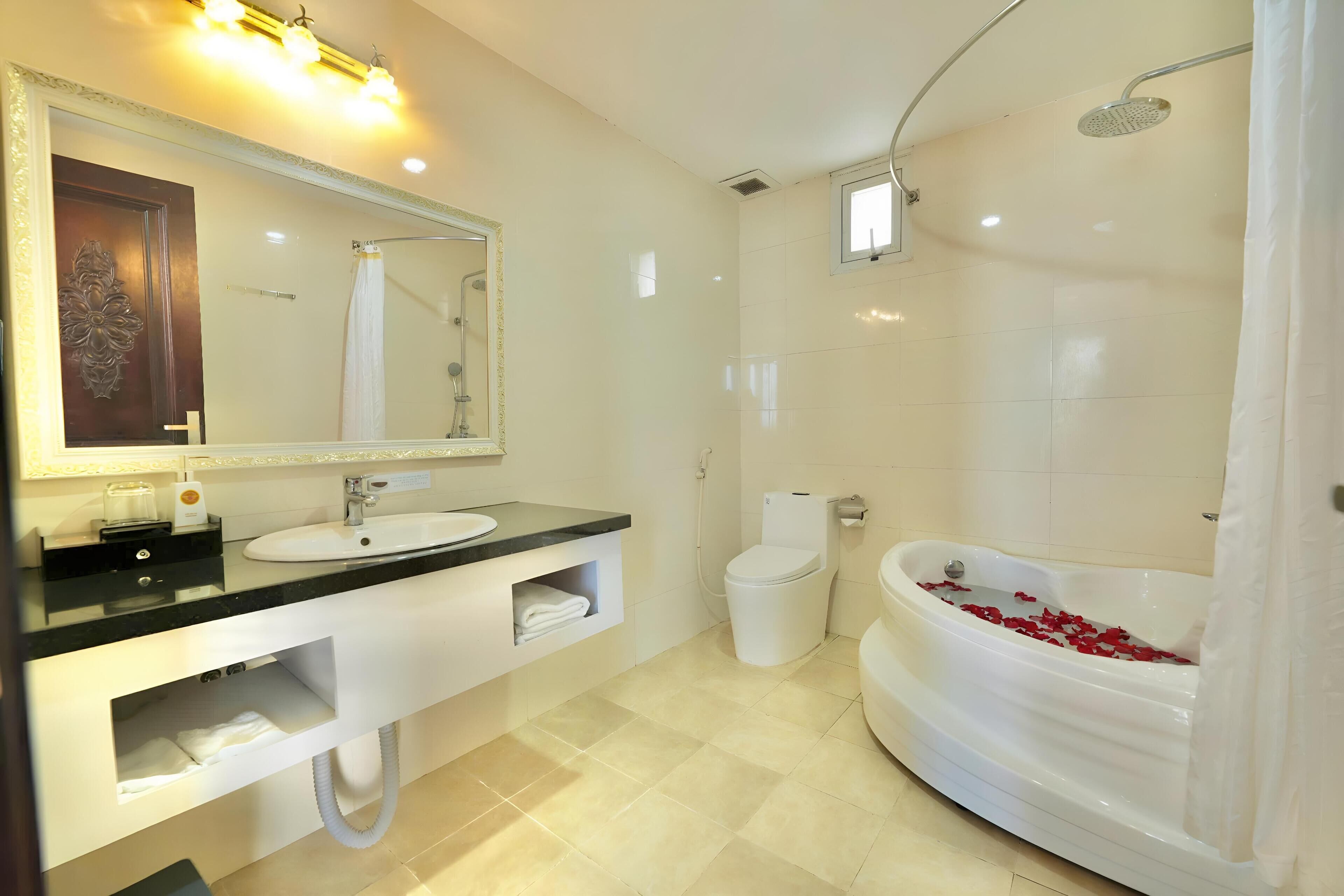 Une salle de bain moderne avec un grand miroir, un lavabo, des toilettes et une baignoire remplie de pétales de rose.