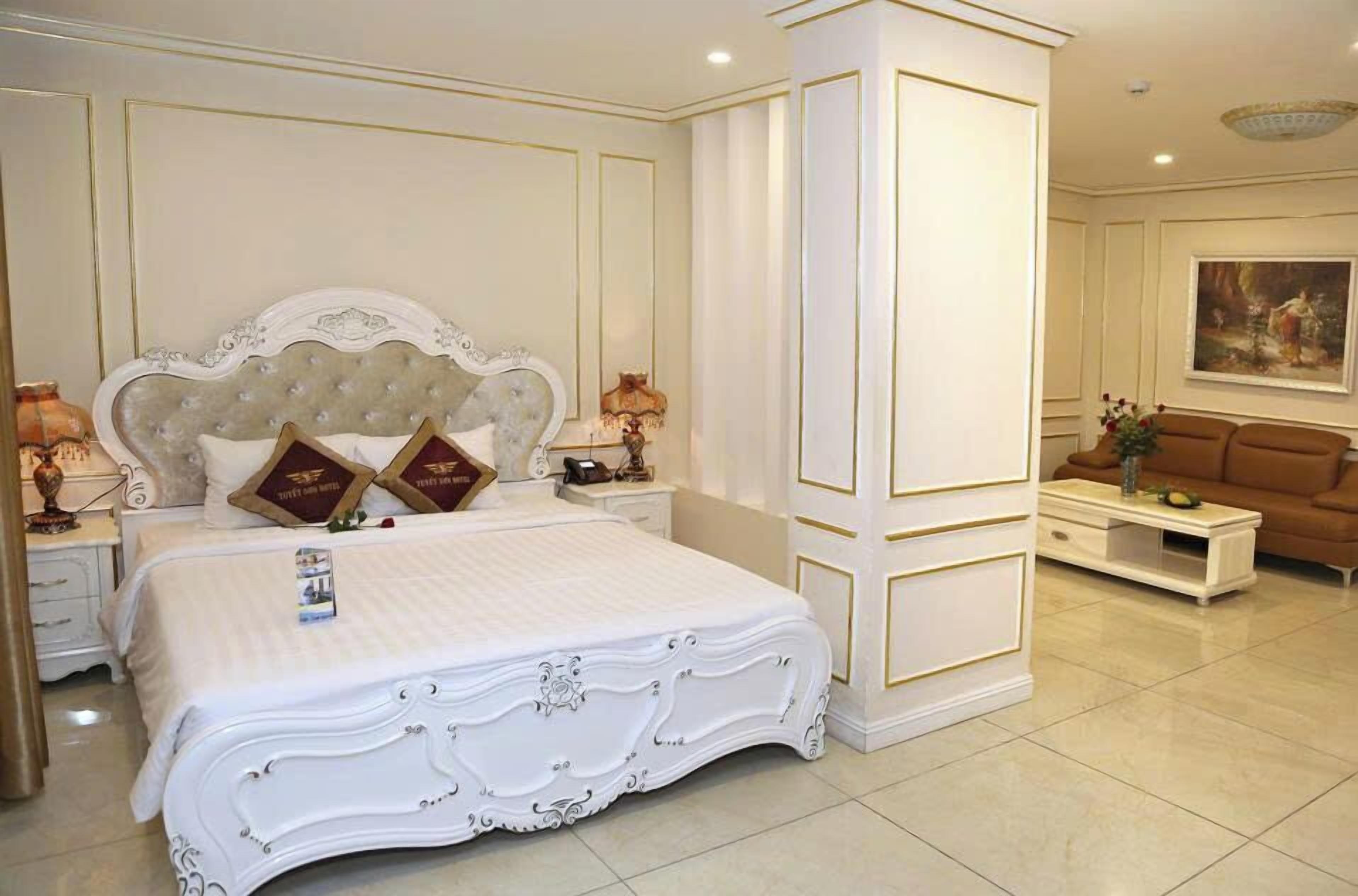 A spacious bedroom with a large bed, a nightstand, a dresser, and a sofa.