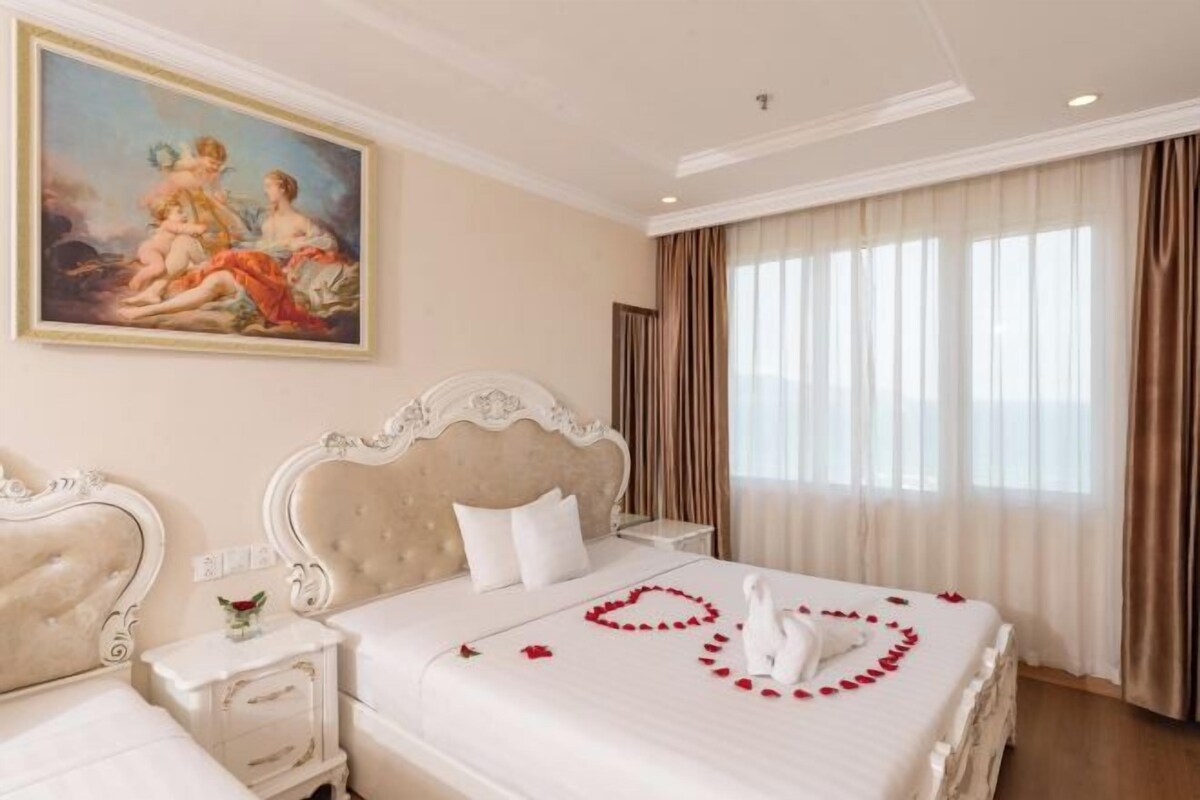 A hotel room with a large bed, a painting on the wall, and a view of the city through the window.