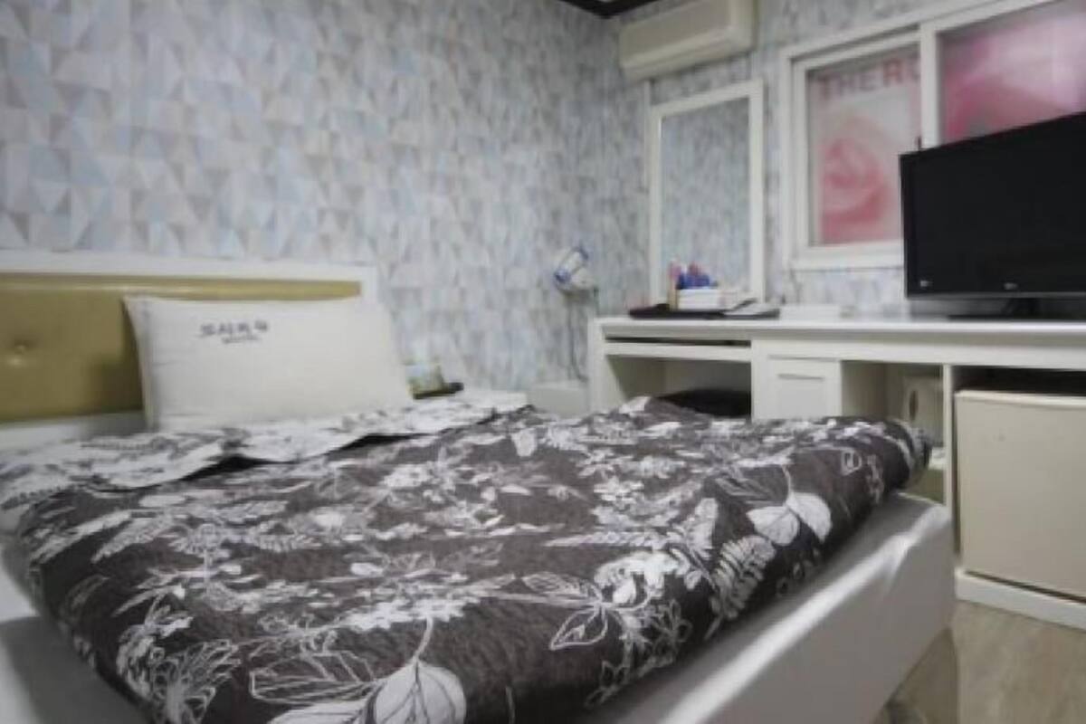 A bedroom with a bed, a desk, a television, and a small refrigerator.
