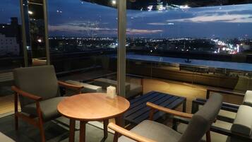 A modern lounge with a panoramic city view, comfortable seating, and a wooden table.