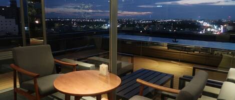 A modern lounge with a panoramic city view, comfortable seating, and a wooden table.