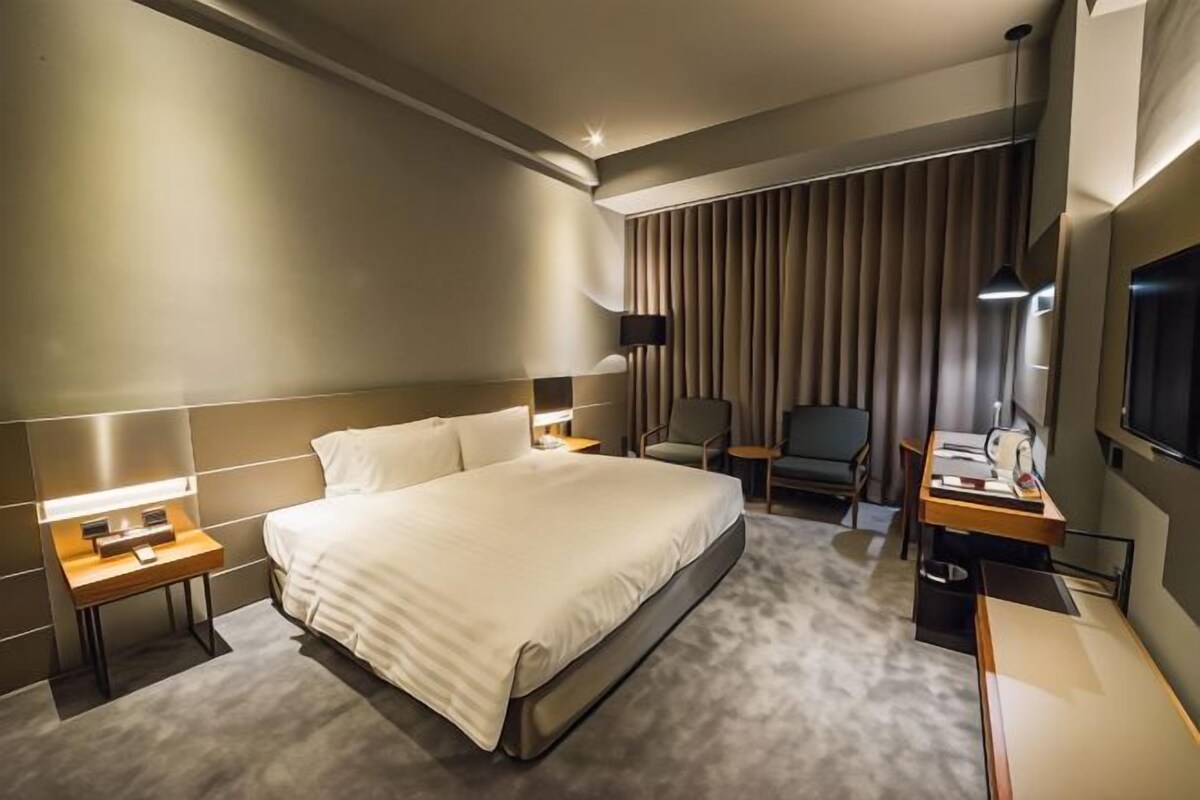 Una habitación de hotel moderna con una cama grande, mesitas de noche, un escritorio, una silla y una televisión.