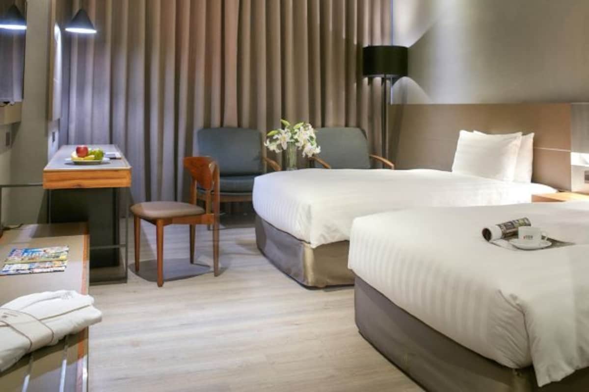Habitación de hotel con dos camas, un escritorio con una silla, una lámpara y un florero con flores.