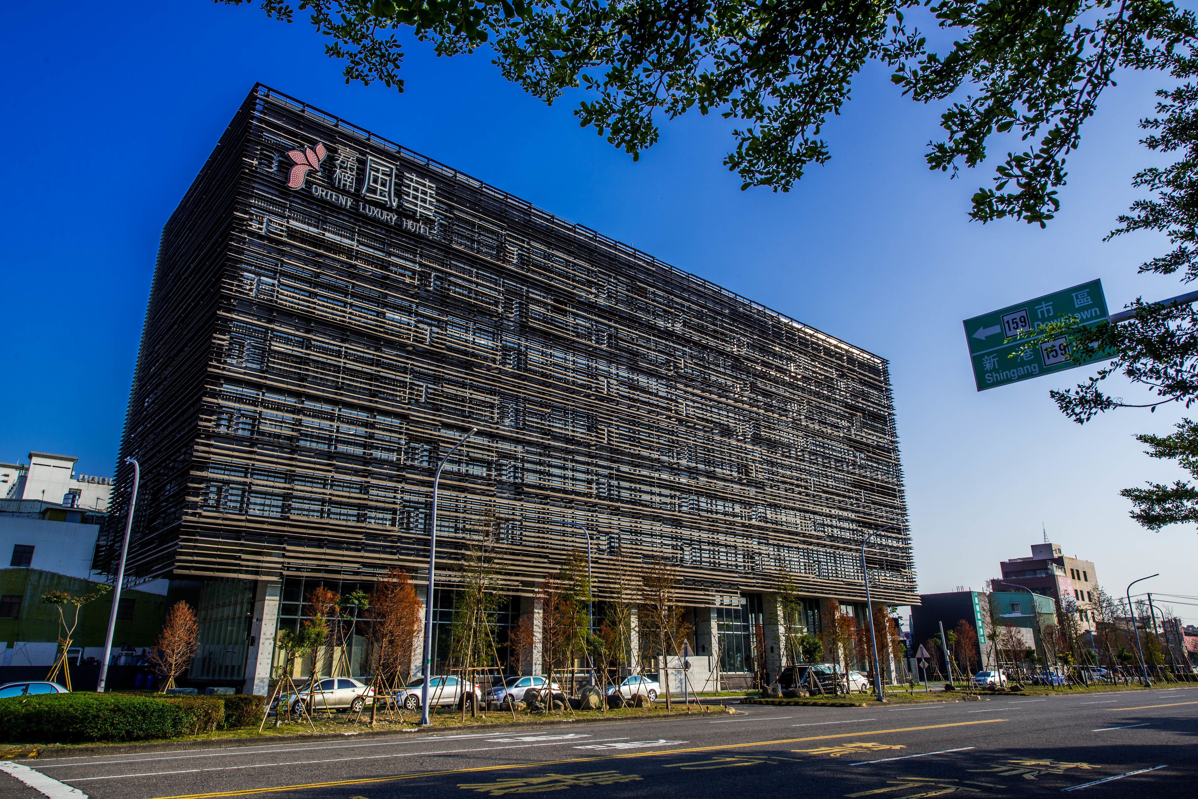 A modern building with a grid-like facade, a sign indicating a nearby location, and parked cars in front.
