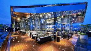 An outdoor lounge area with seating and tables, surrounded by glass walls and a wooden deck. - Orient Luxury Hotel (Chiayi City)