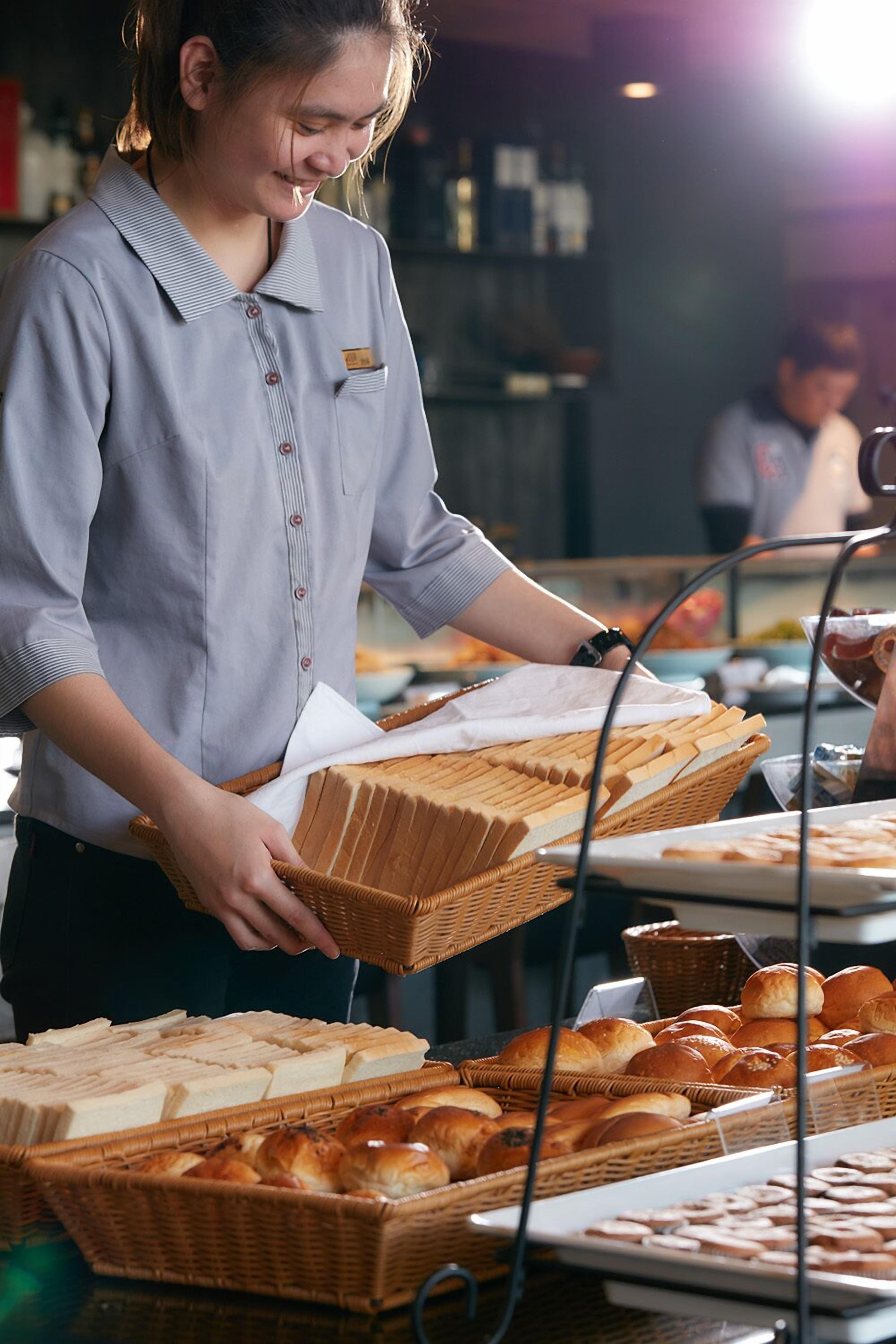 A person arranging bread baskets on a table with various types of bread.