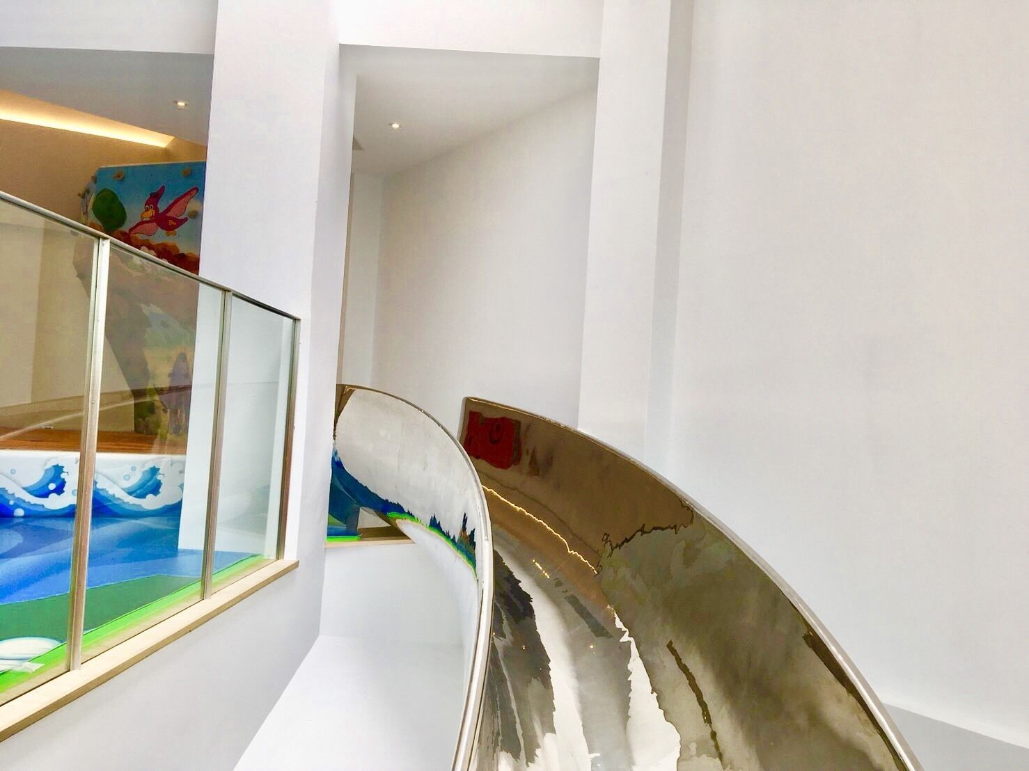 A modern interior with a glass railing, a curved wall with a wave pattern, and a staircase.
