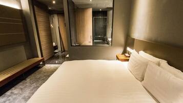 Een moderne hotelkamer met een groot bed, een bankje, een nachtkastje en een spiegel.