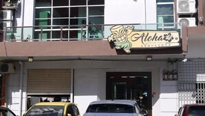 A building with a sign for 'Alchoa' and a parked car in front. - Aloha Capsule Hostel (Semporna)