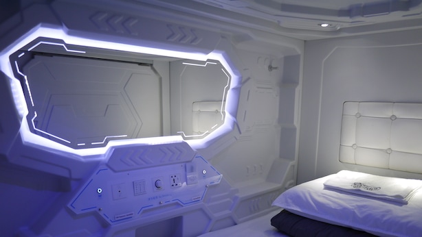A modern, minimalist bedroom with a geometric wall design, a bed with a white headboard, and a control panel with a 'No Smoking' sign. - Aloha Capsule Hostel (Semporna)