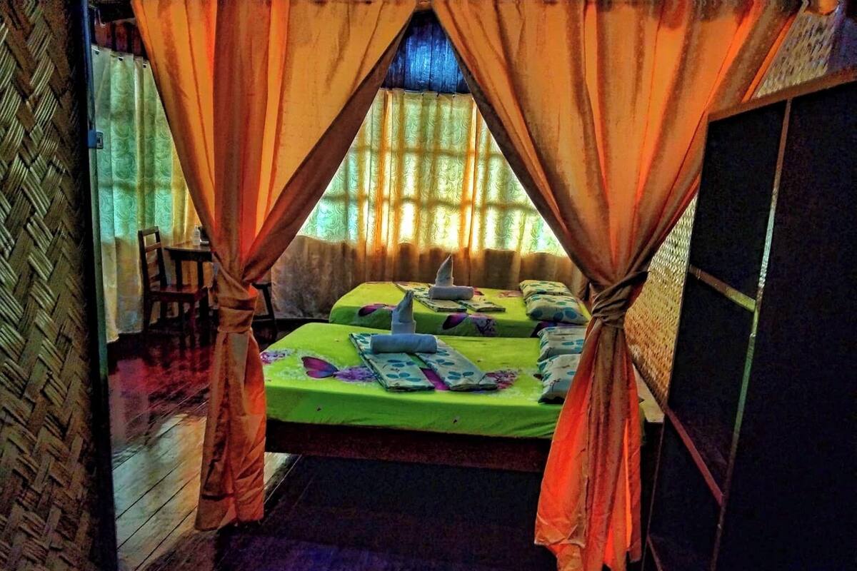 Ein Zimmer mit zwei Betten, jeweils mit grüner Bettdecke und Kissen, und orangefarbenen Vorhängen.