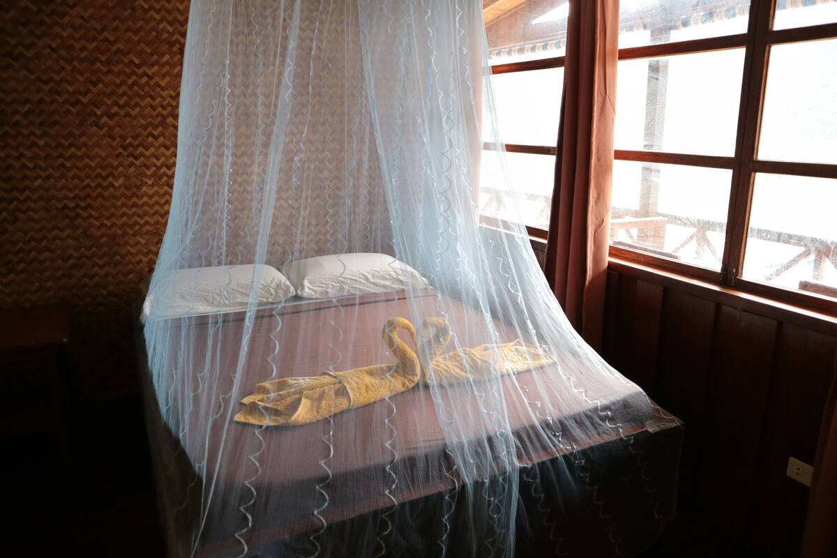 Ein Bett mit Moskitonetz, Holzwänden und einem Fenster mit Blick.