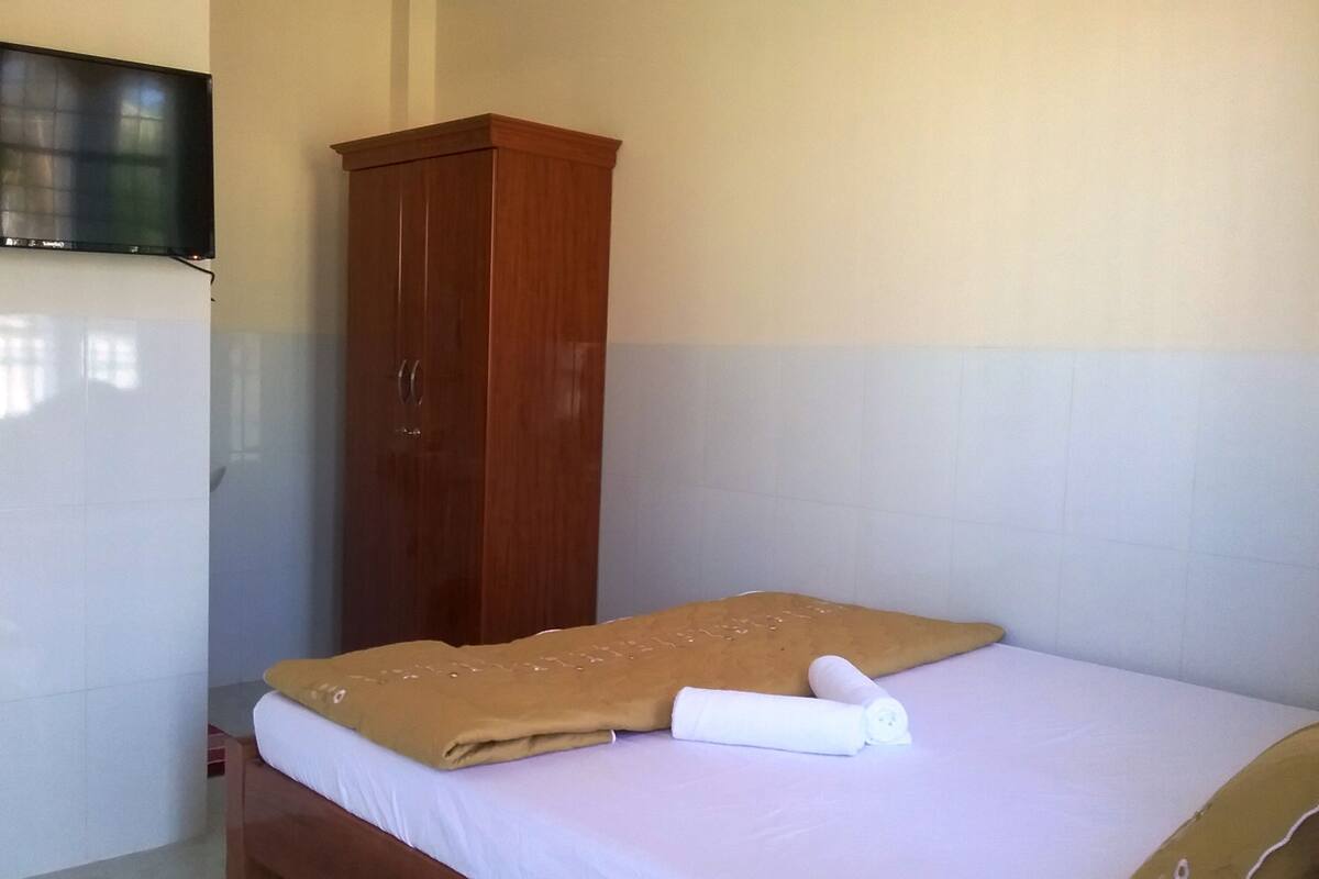 A bedroom with a bed, a wooden wardrobe, and a television mounted on the wall.
