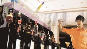A bar area with multiple bottles and glasses, a person in an orange shirt, and a ceiling with a decorative light fixture. - Dongguan Silver Holiday Hotel (Dongguan)