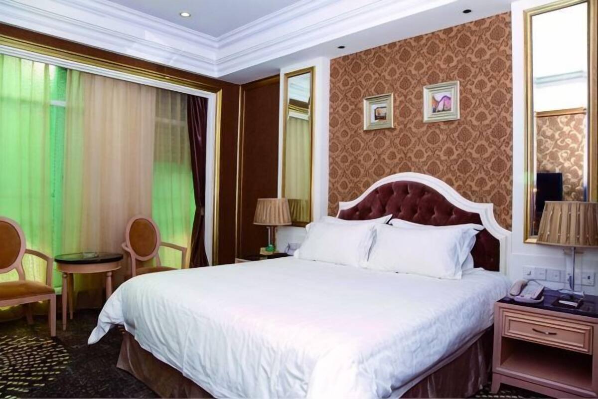 A hotel room with a large bed, a desk, a chair, a mirror, and a window with curtains.