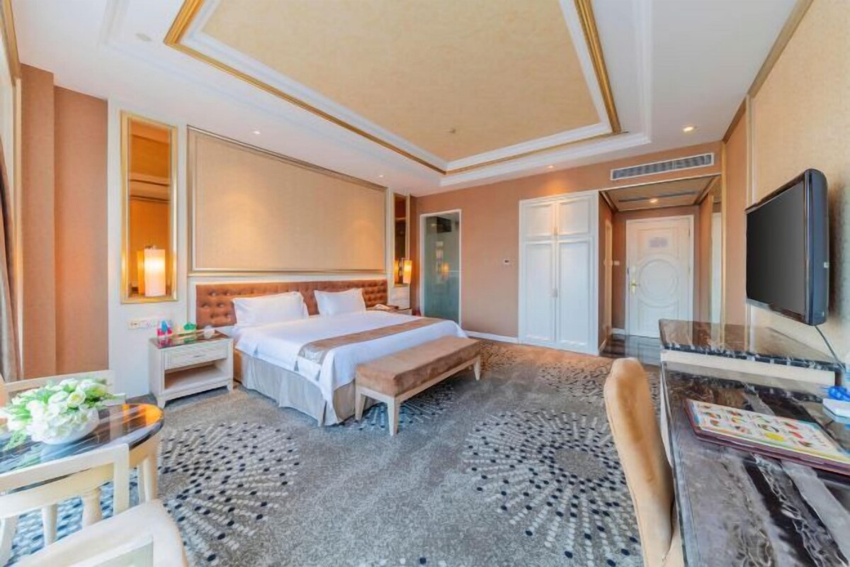 A hotel room with a large bed, a desk with a computer, a TV, and a bathroom with a mirror and toilet.