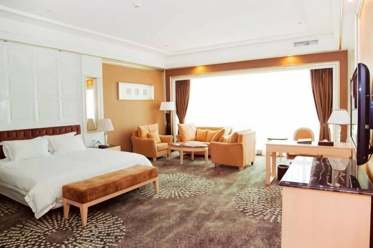 A hotel room with a bed, a sofa, a desk, and a TV.