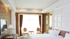 A hotel room with a large bed, a desk with a lamp, two chairs, a television, and a large window with curtains. - Dongguan Silver Holiday Hotel (Dongguan)
