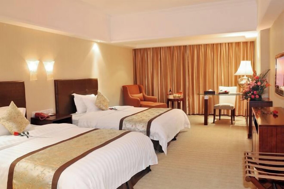 Ein Hotelzimmer mit zwei Betten, einem Schreibtisch, einem Sessel und einem Fernseher.