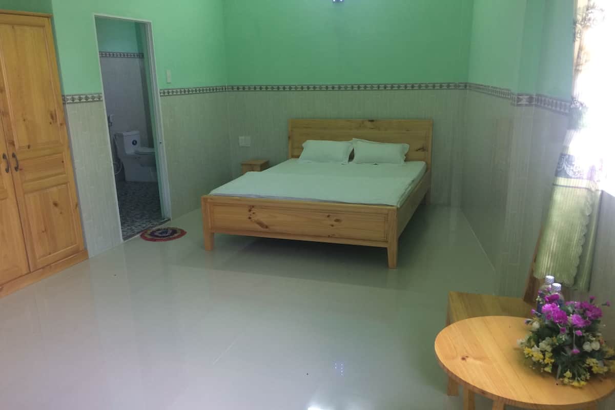 Un dormitorio con una cama de madera, una mesita de madera con un florero y un armario de madera.