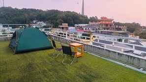 A rooftop with a green tent, a folding chair, and a small table. There are solar panels and a traditional building in the background. - Y Thu Guesthouse (Phu Quoc)