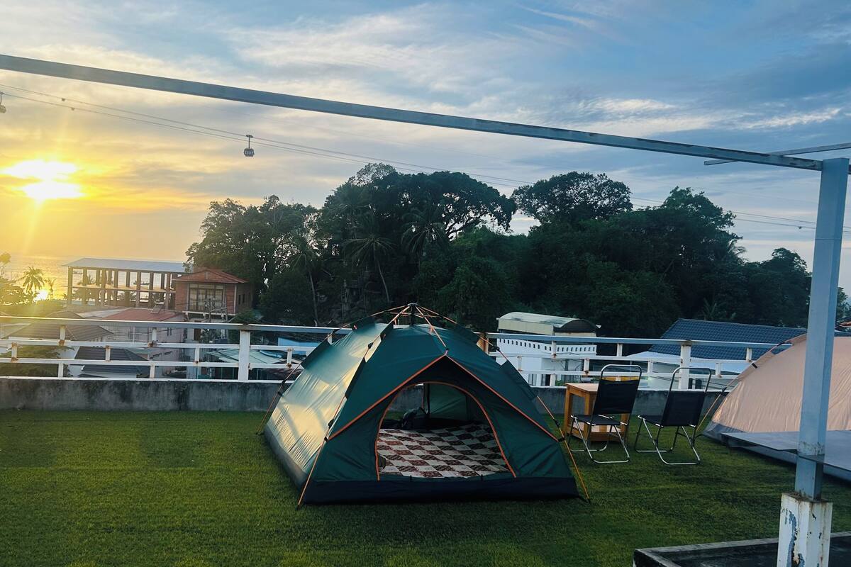 Una carpa verde sobre un césped, con vista al atardecer y árboles en el fondo.