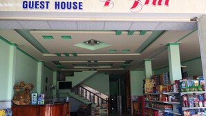 The entrance of a guest house with a staircase leading to the upper floor, a reception desk, and shelves stocked with various products. - Y Thu Guesthouse (Phu Quoc)
