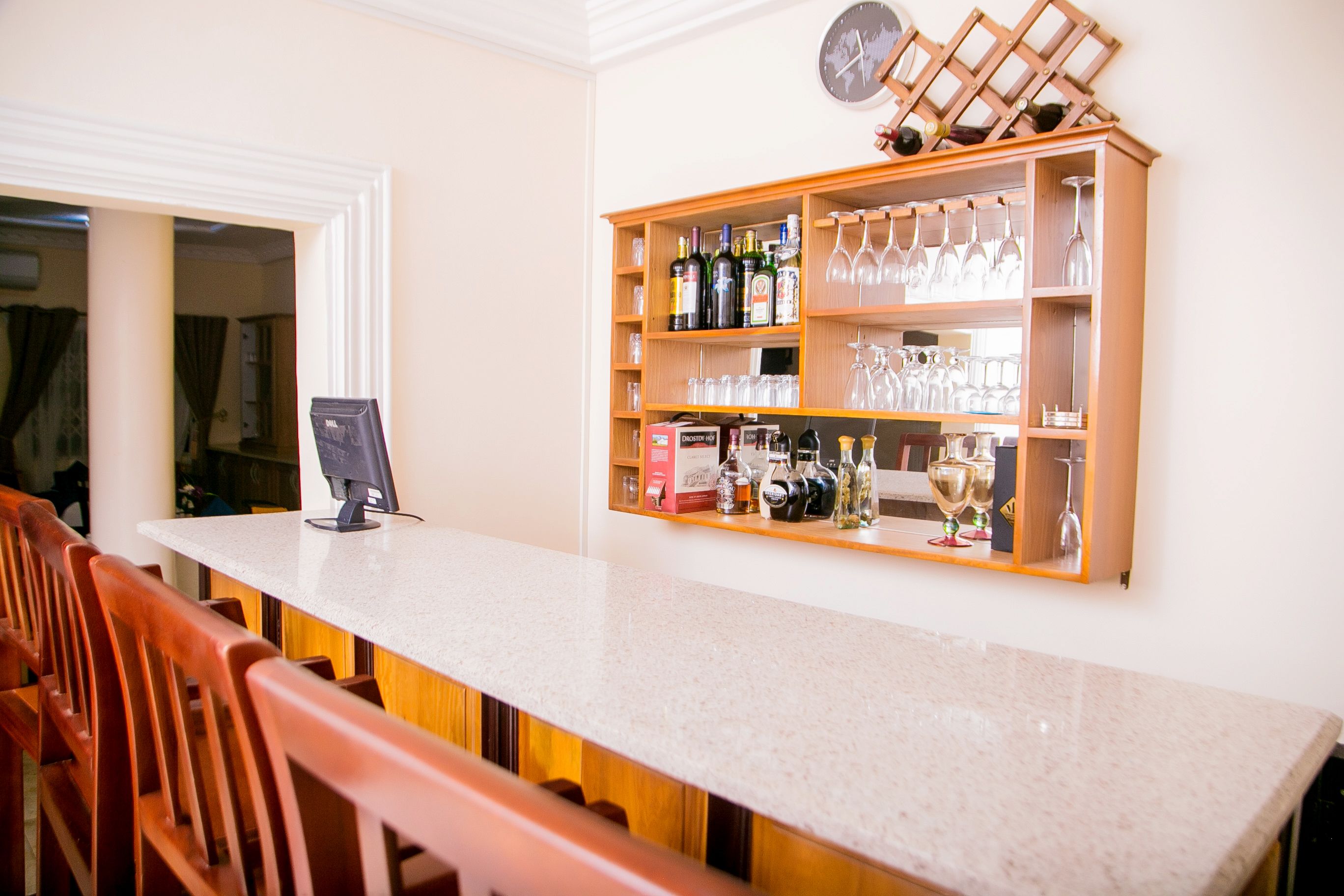 A bar area with a long counter, wooden chairs, a wine rack, and a clock on the wall.