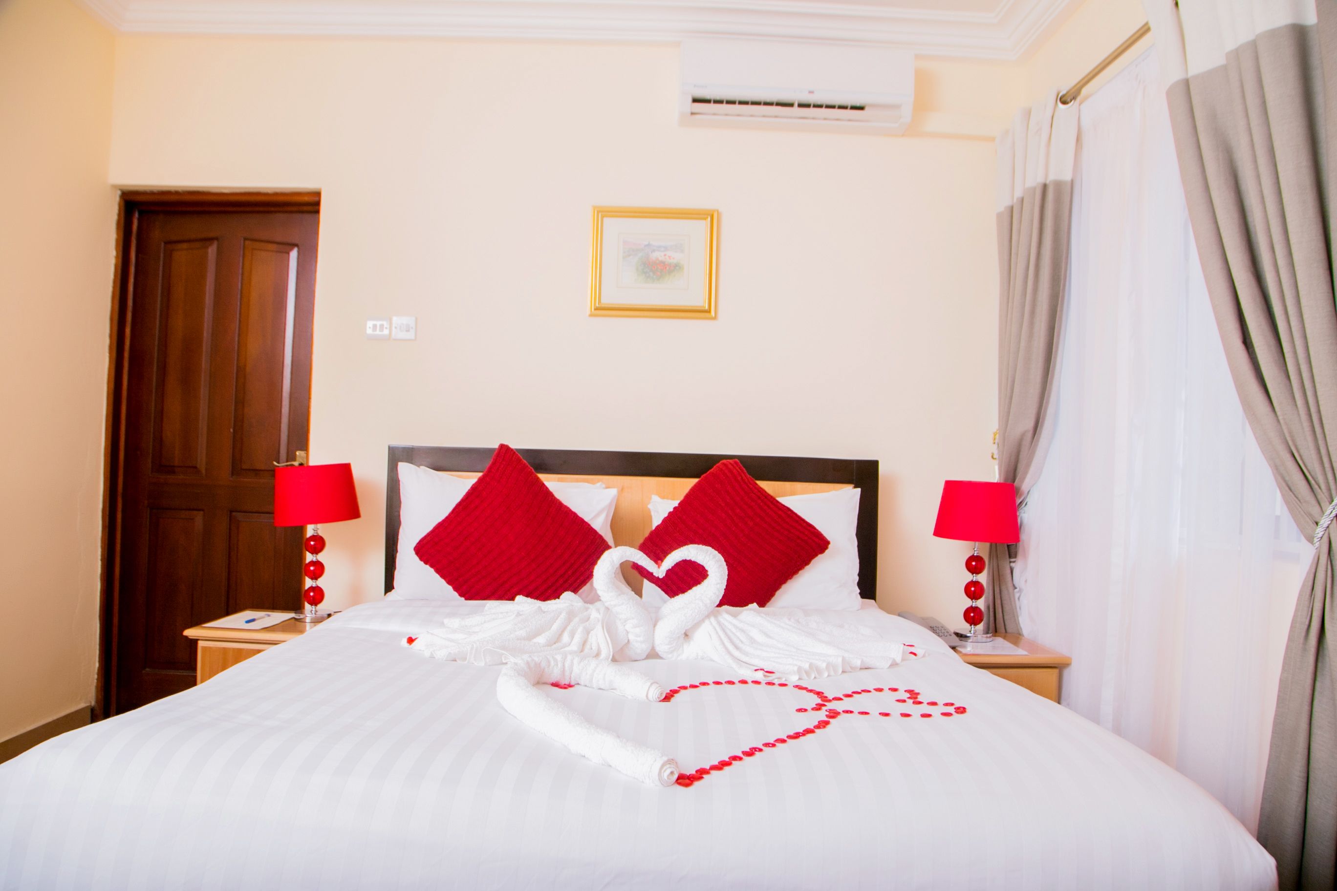 Habitación de hotel con una cama bien hecha, almohadas rojas y una disposición de toallas con forma de corazón.