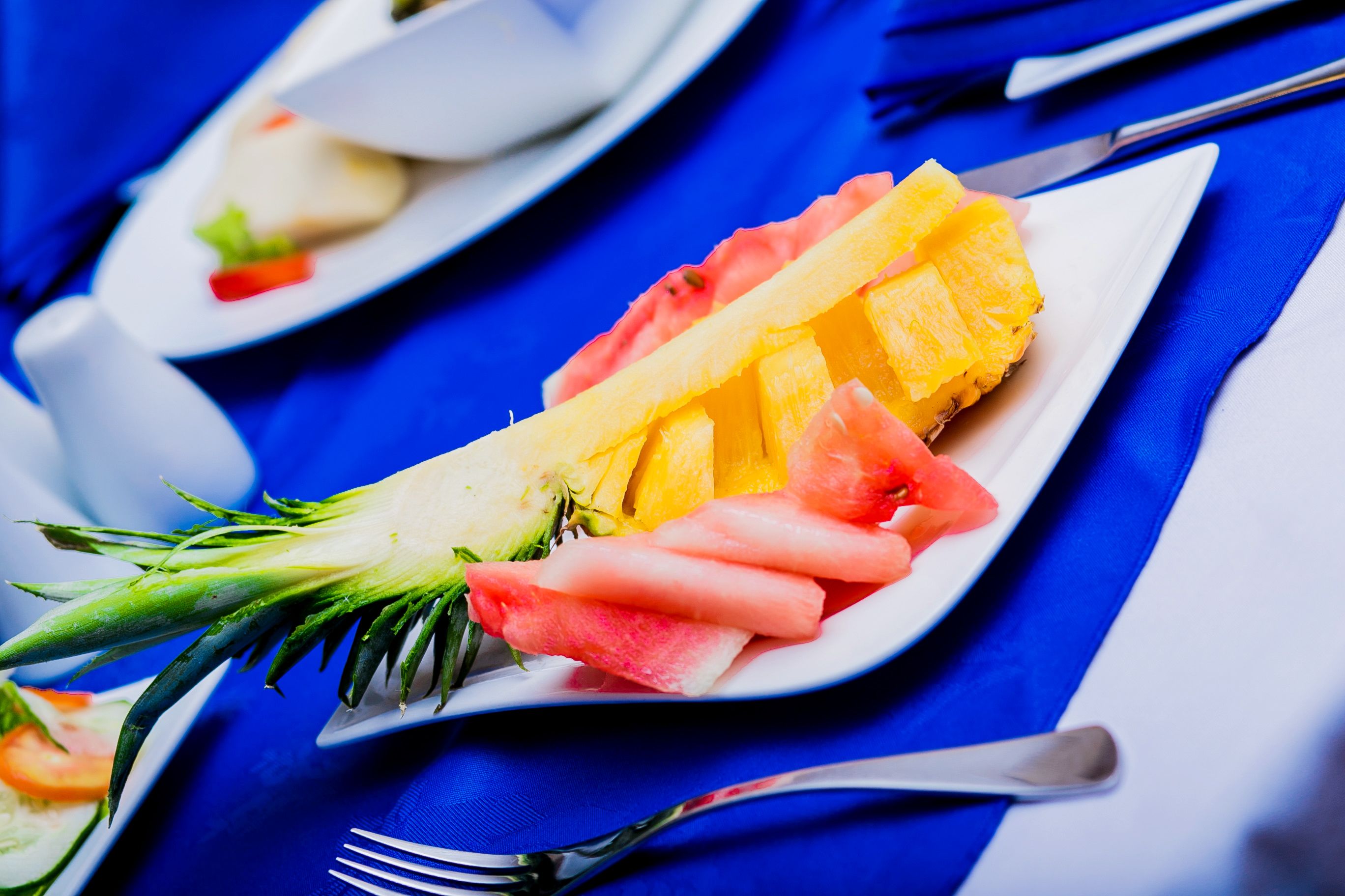 A plate with pineapple, watermelon, and a vegetable, possibly a radish, on a blue tablecloth.