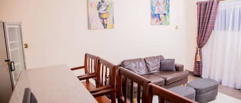 A modern living room with a dining area, featuring a sofa, chairs, a coffee table, and artwork on the walls.