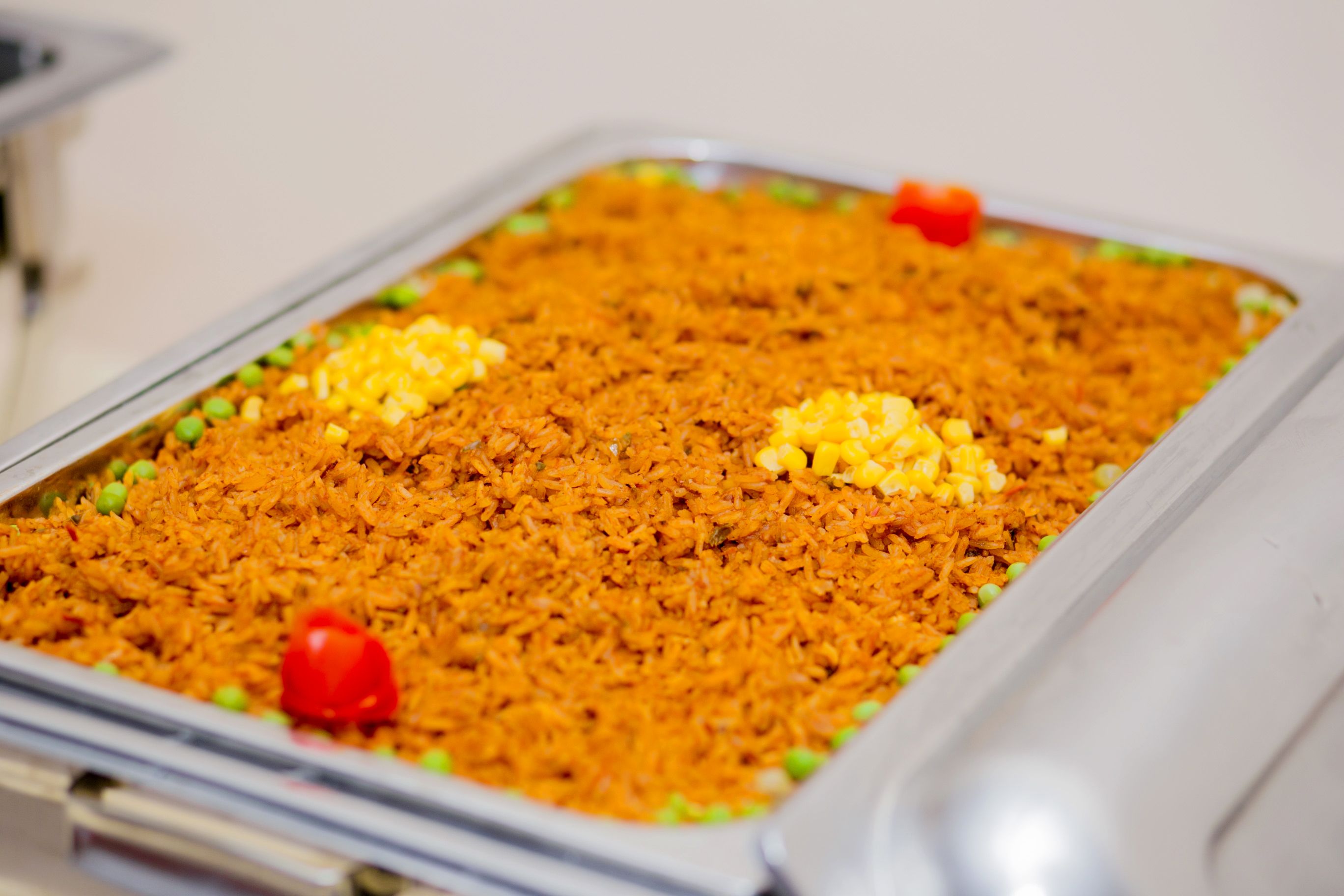Una bandeja de arroz con guisantes y granos de maíz, adornada con un tomate cherry y una cucharada de mantequilla.