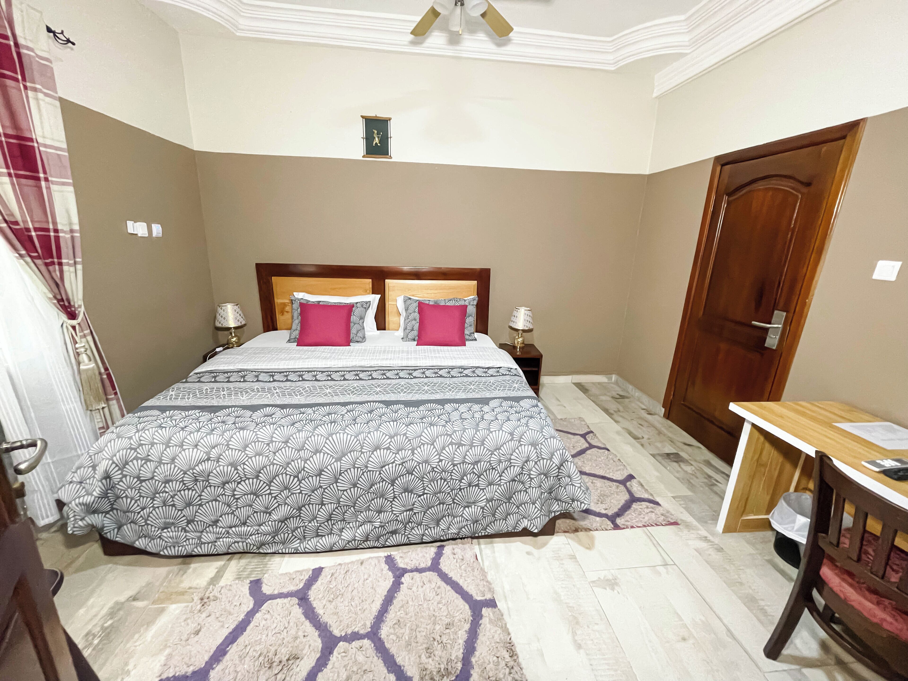 Een slaapkamer met een groot bed, twee nachtkastjes met lampen, een houten deur en een klein raam met een afbeelding.