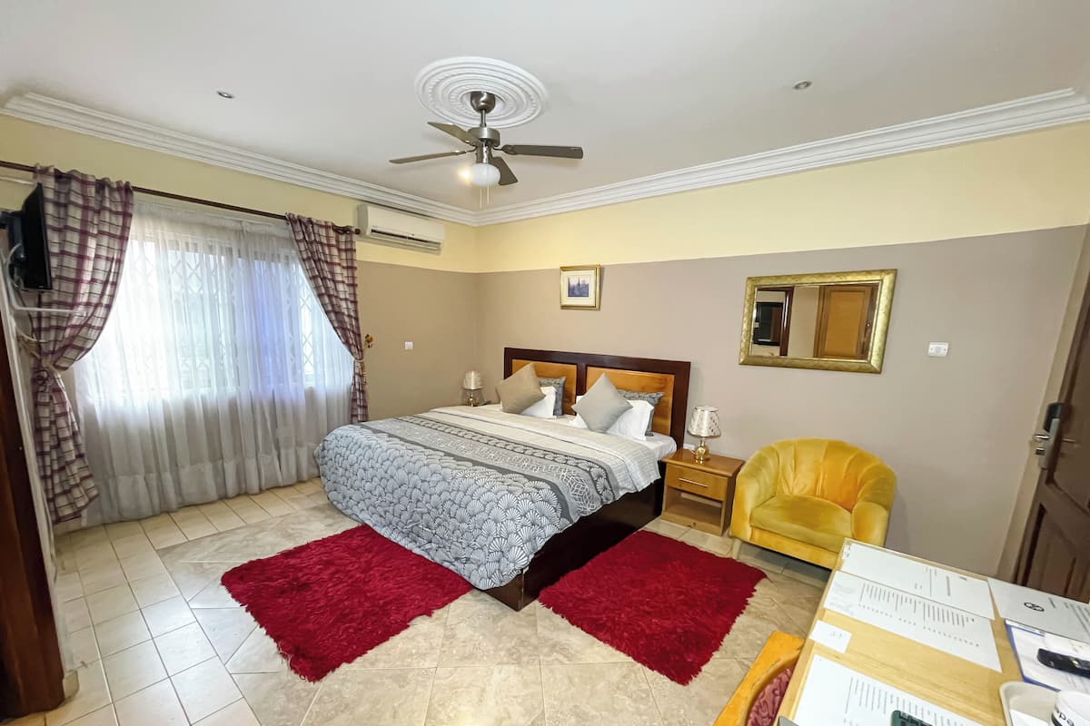 A hotel room with a bed, a desk, a chair, a ceiling fan, and a window with curtains.