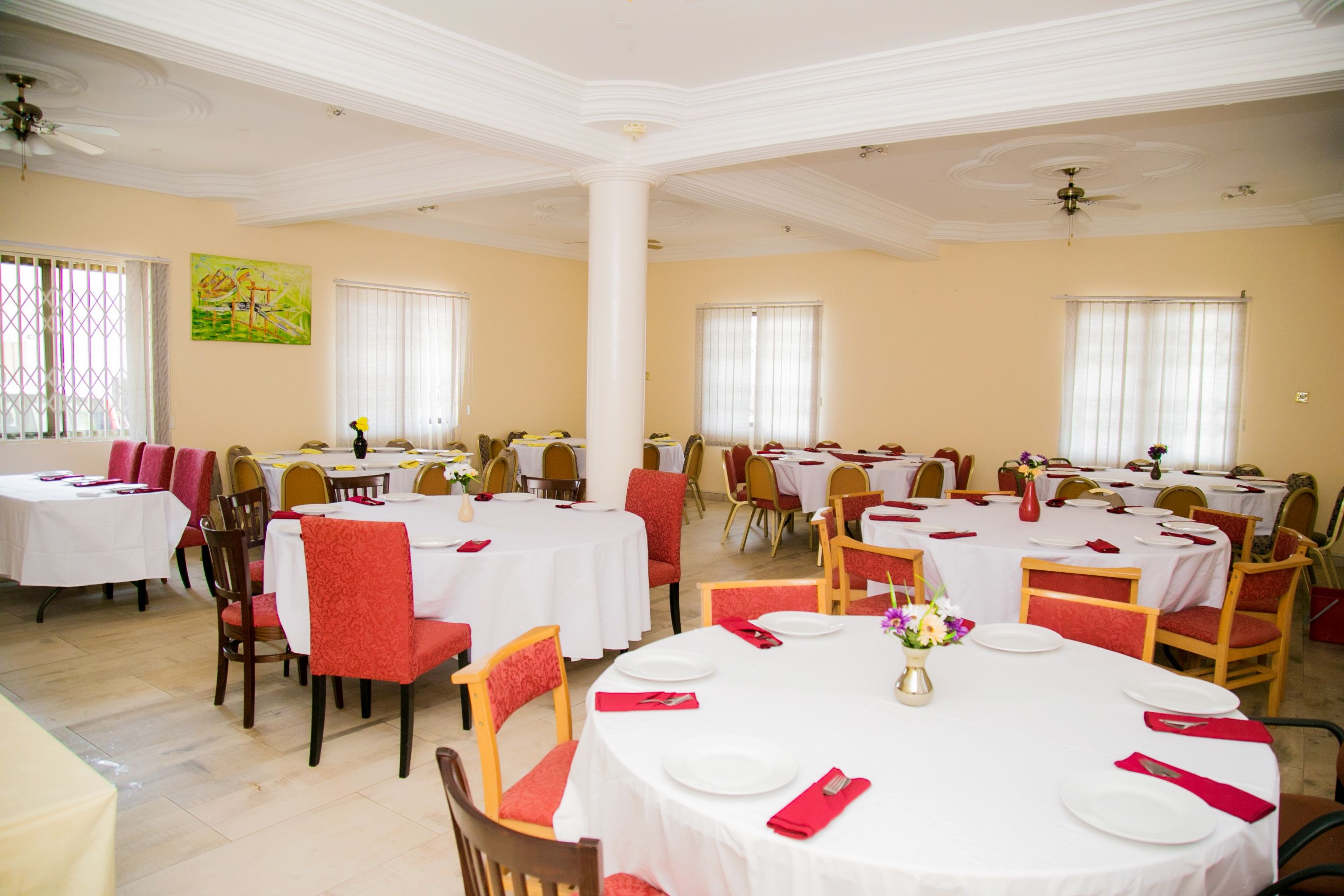 A dining area with multiple round tables, each set with white tablecloths, red napkins, and floral centerpieces.