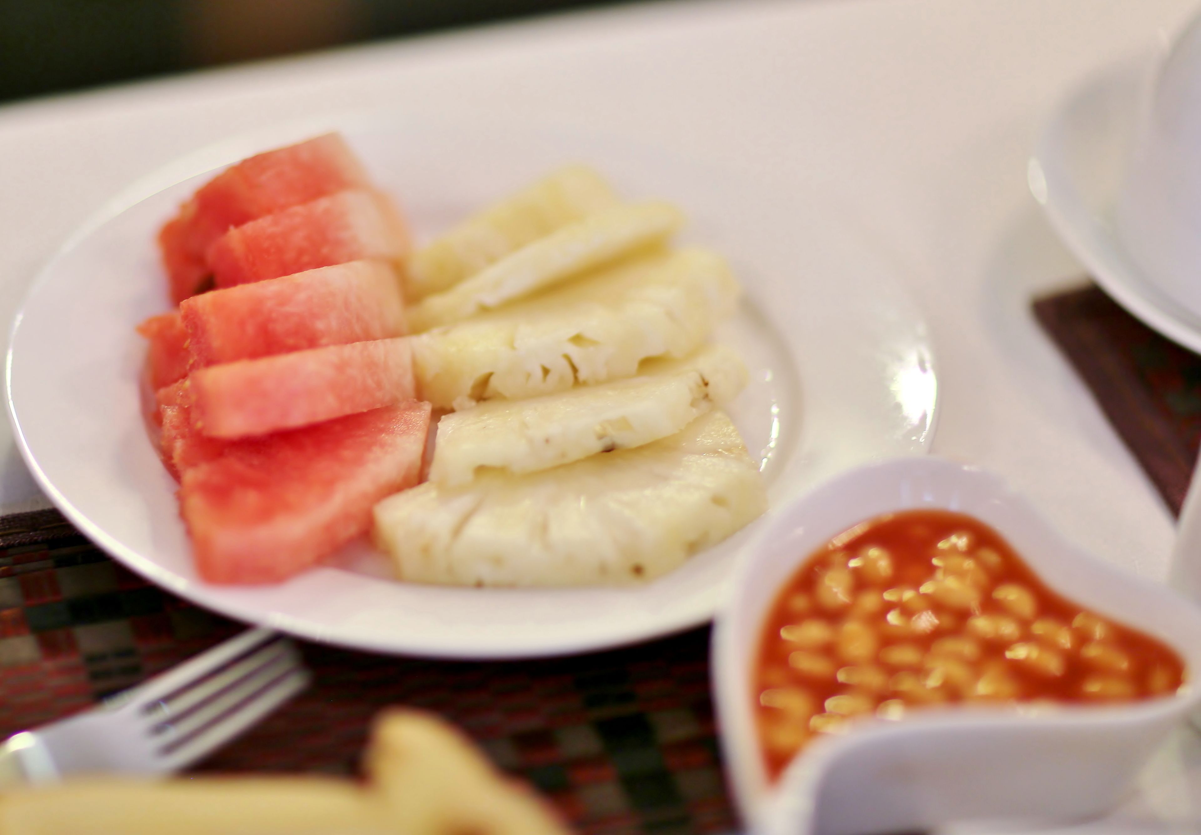 A plate with sliced watermelon and pineapple, and a small bowl of beans.