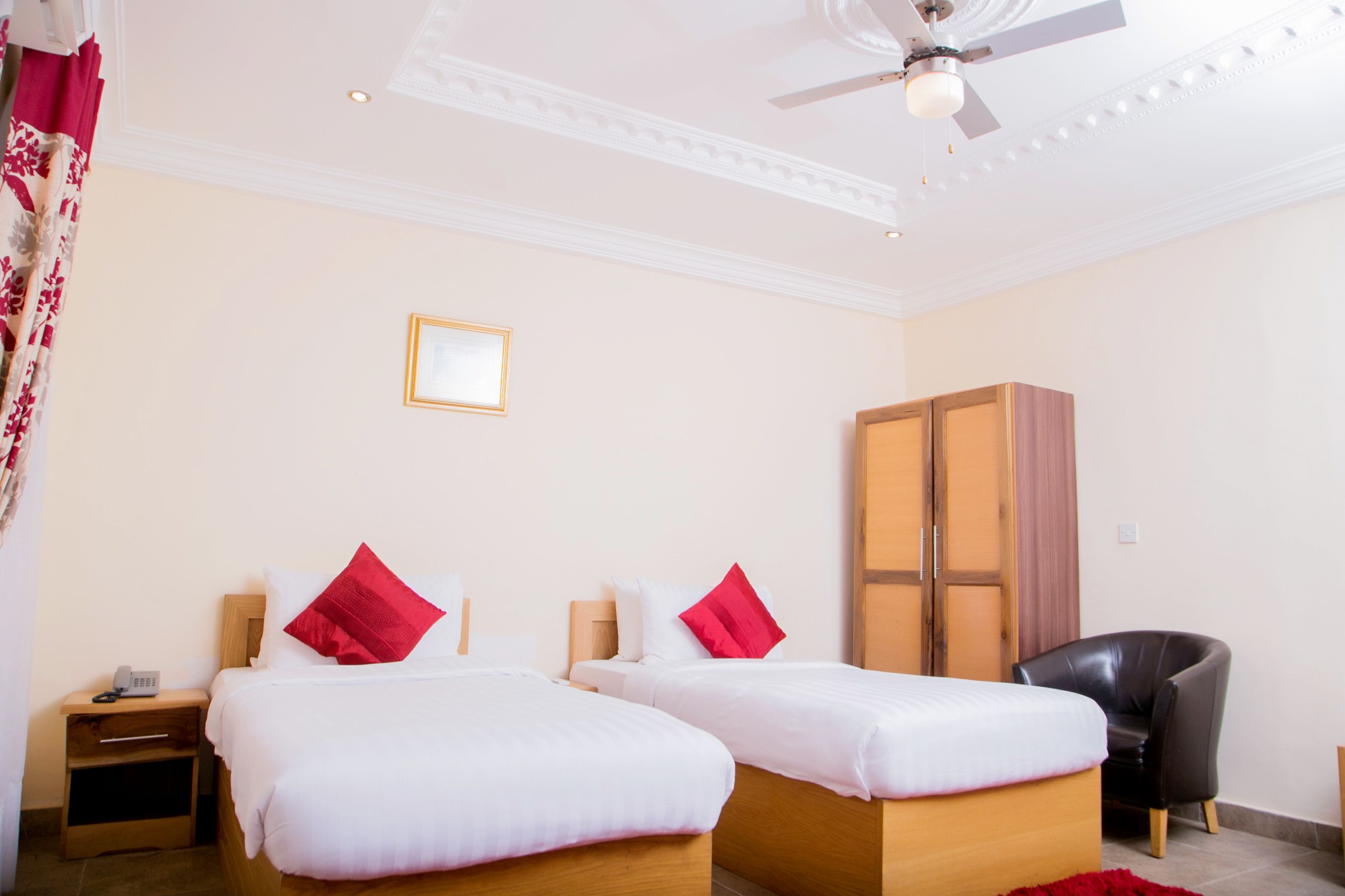 Une chambre d’hôtel avec deux lits, une armoire, une chaise et un ventilateur de plafond.