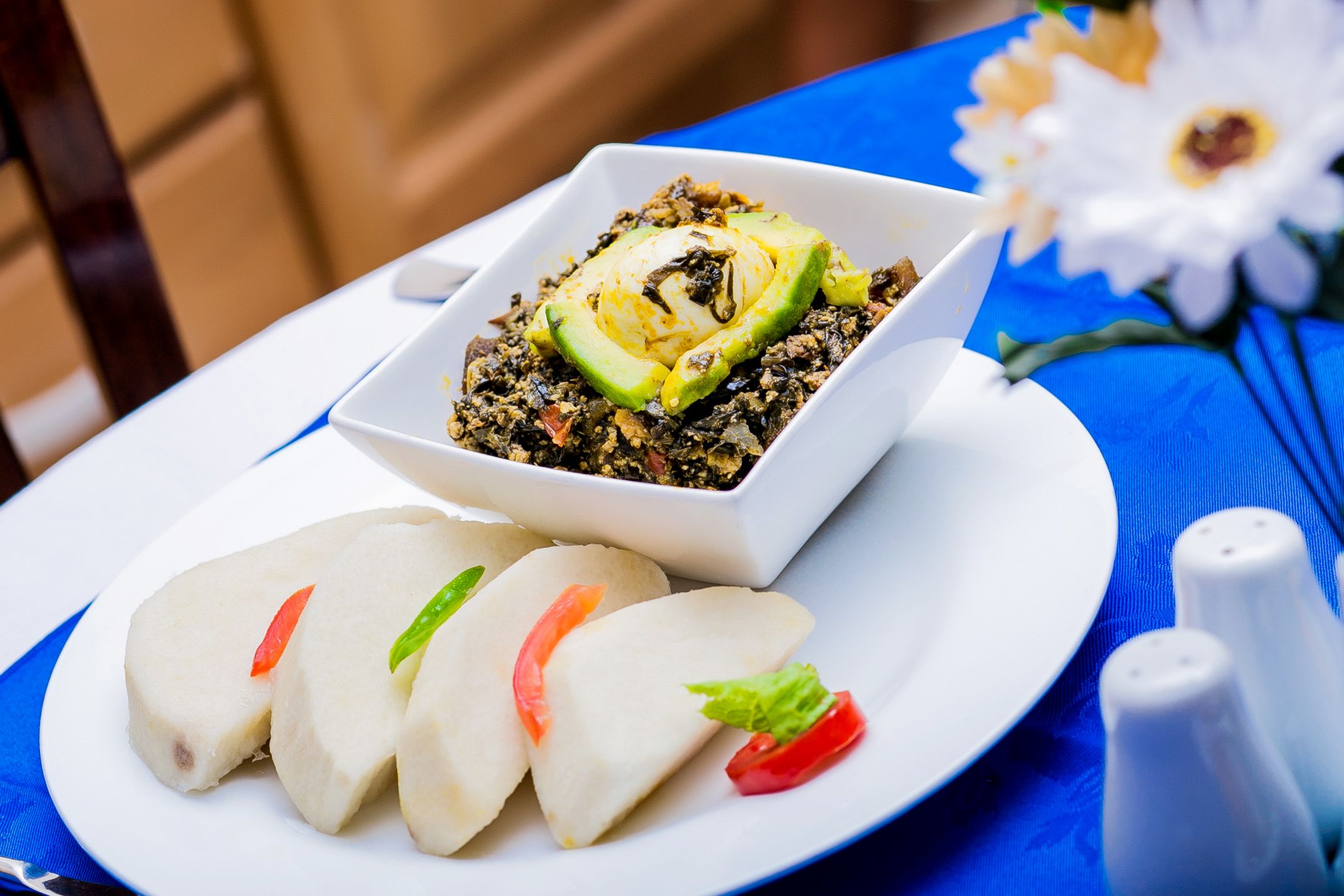 A white plate with a bowl of food, a white plate with sliced items, and a blue tablecloth.