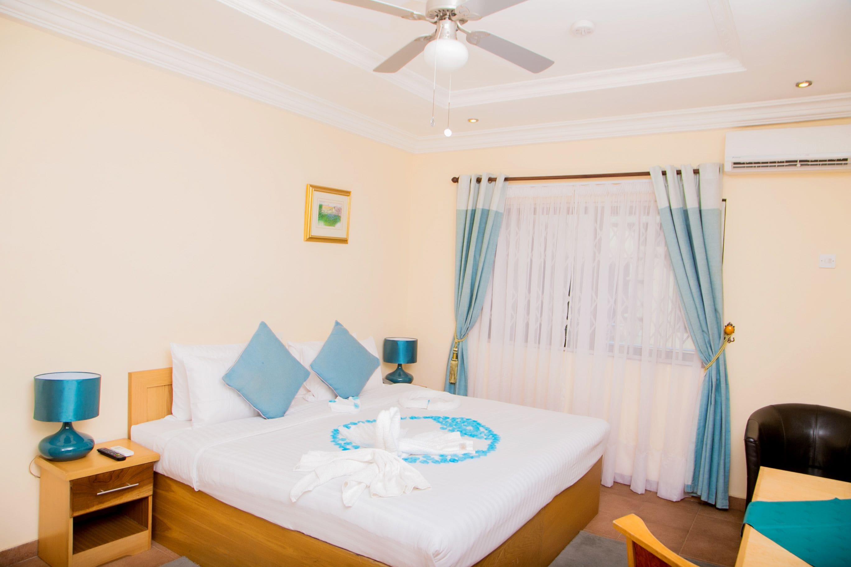 A hotel room with a bed, two bedside tables with lamps, a chair, a ceiling fan, and a window with curtains.
