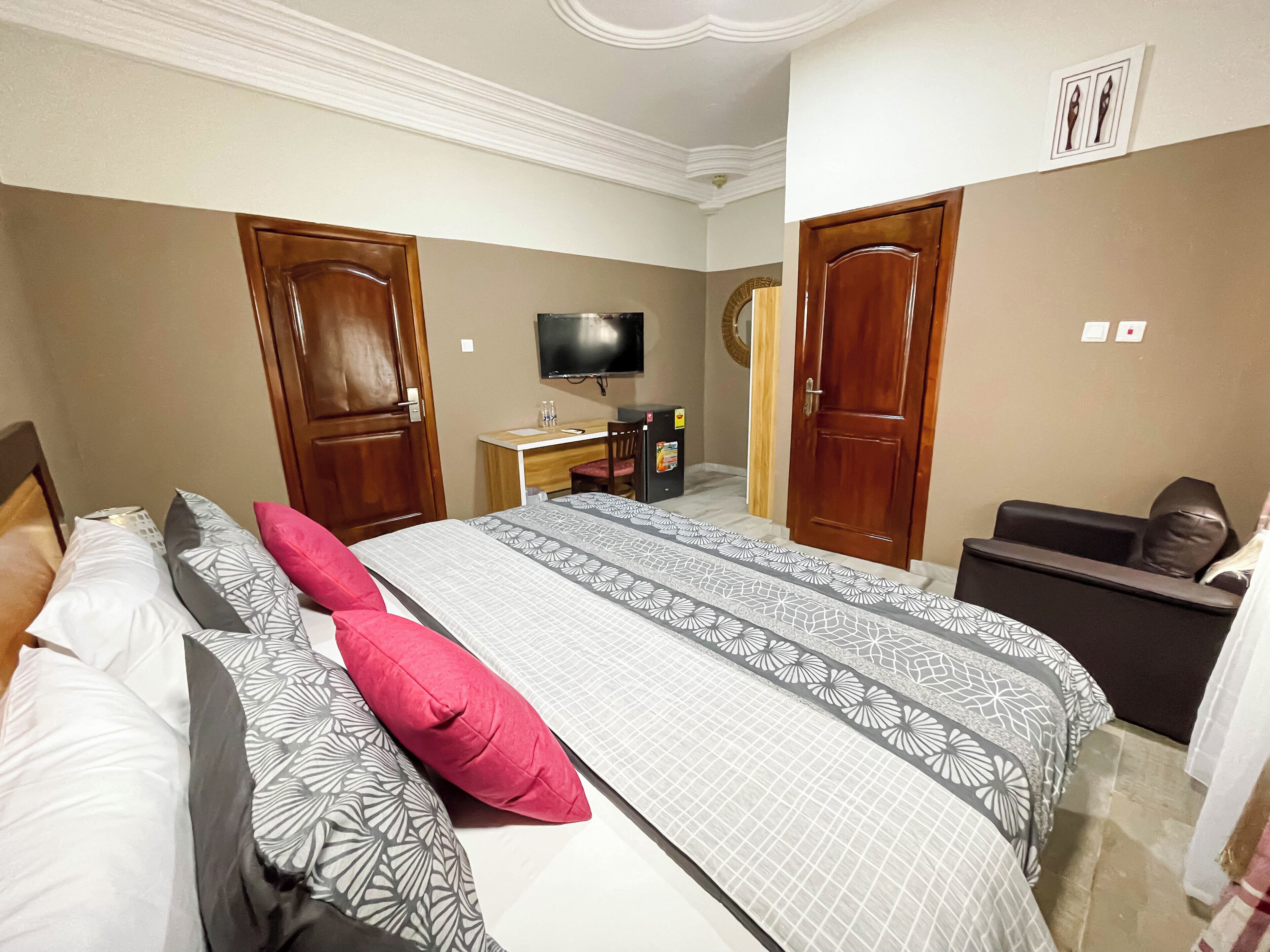A hotel room with a bed, a desk, a chair, a TV, and two doors.