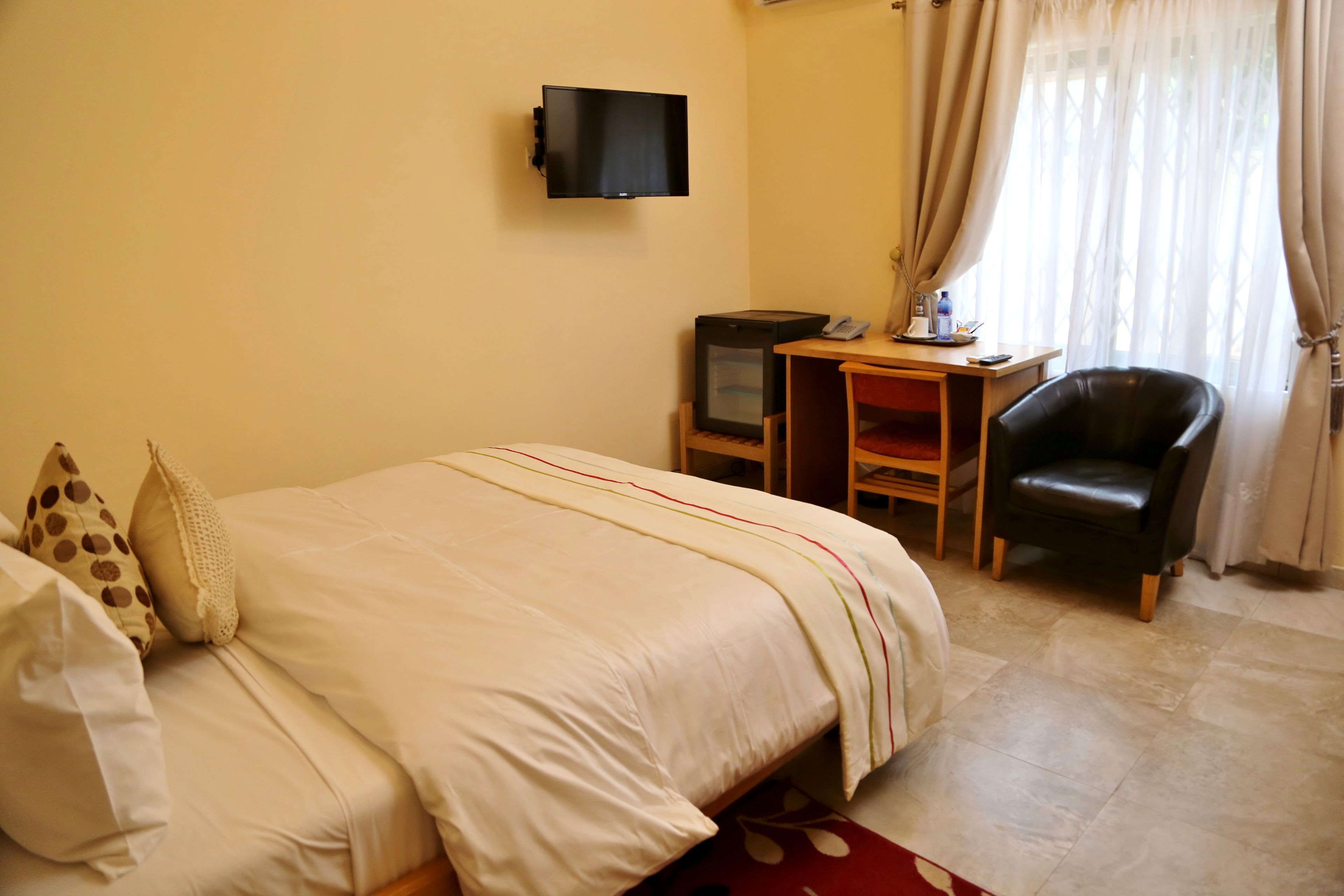 A hotel room with a bed, a desk with a television, a chair, and curtains.